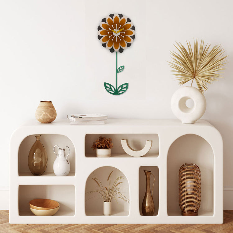Decorative pendulum wall clock shaped like a flower in orange and brown with green pendulum.